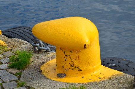 Gelber Poller am Hafen mit einer rauen Oberfläche neben Wasser und Steinen.