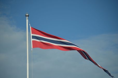 Flagge Norwegens mit rot-blauen Streifen, weht vor blauem Himmel.