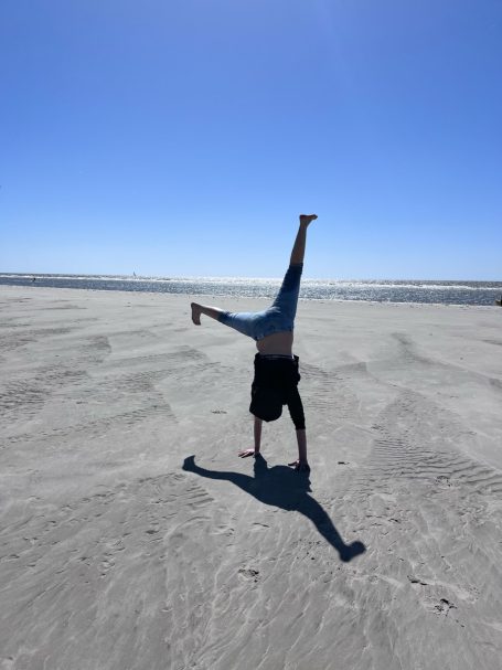 Person macht einen Handstand am Strand bei sonnigem Wetter.