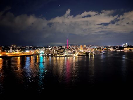 Stadtansicht bei Nacht mit buntem Lichtspiel und reflektierendem Wasser.