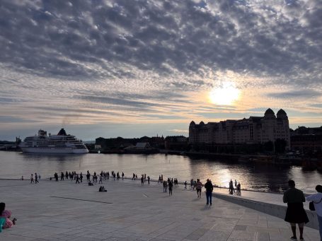 Sonnenuntergang über einem Fluss mit Menschen und einem Schiff im Hintergrund.