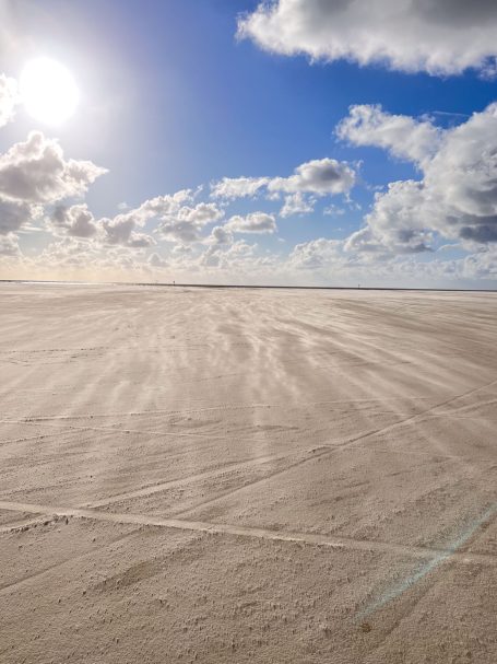 Weitläufiger Sandstrand unter einem sonnigen Himmel mit einigen Wolken.