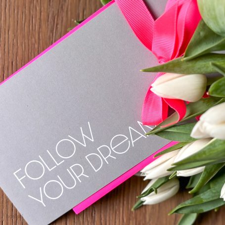 Graue Karte mit Aufschrift "Follow Your Dreams" und weißen Tulpen mit pinkem Band.