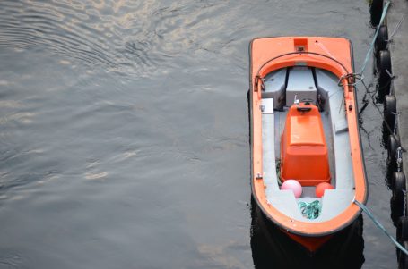 Orangenes Boot mit Ausrüstung und zwei pinken Bällen im ruhigen Wasser.