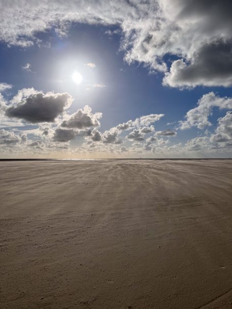 Sonniger, bewölkter Himmel über einer großen, offenen Sandfläche.