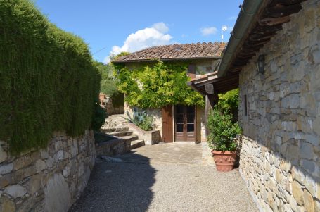 Pflasterweg zwischen Steinhäusern mit Bepflanzung und blauen Himmel.