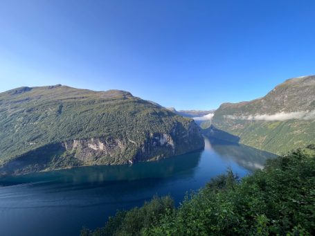 Blick auf einen ruhigen Fjord umgeben von Bergen und klarem blauen Himmel.