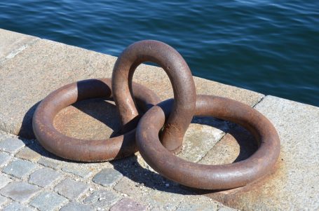 Drei verbundene, rostige Metallringe auf einem Steg am Wasser.