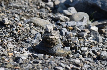 Steinerne Skulptur aus verschiedenen Gesteinen auf einem kiesigen Untergrund.
