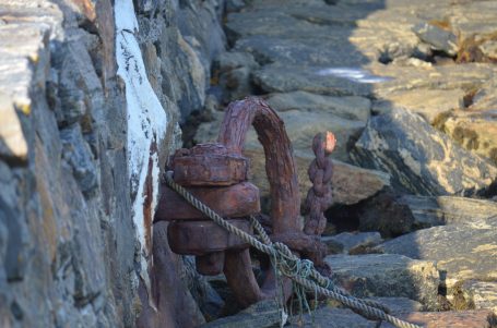 Rostige Kette und Haken an einem steinigen Ufer.