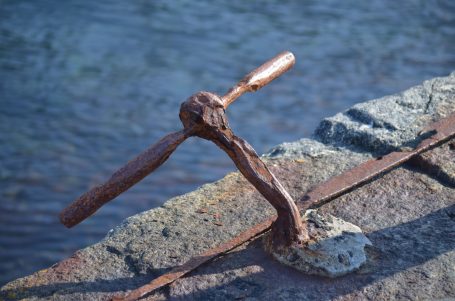 Eisenanker mit einem Holzgriff, befestigt an einem Steinpfad am Wasser.