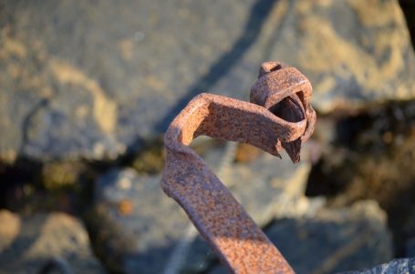 Rostiges Metallstück, das aus dem Boden ragt, umgeben von Steinen und Wasser.