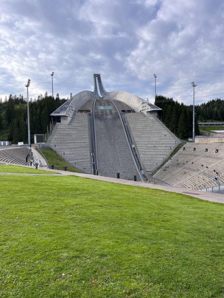 Skisprungschanze mit steil geneigtem Aufsprunghang und grüner Rasenfläche im Vordergrund.